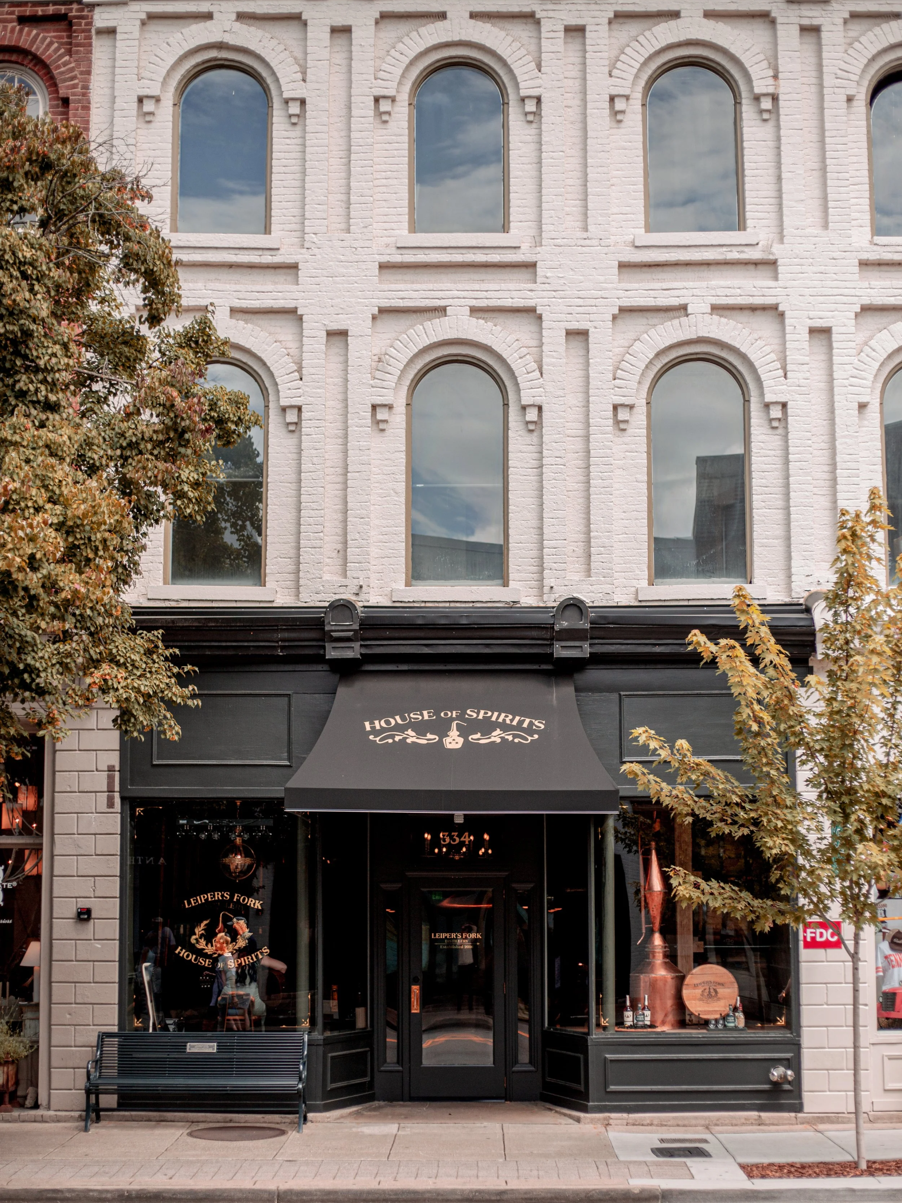 House Of Spirits Ila Bridal Facade of a pale brick building with arched second-floor windows and a black storefront awning reading 'House of Spirits' over the entrance.