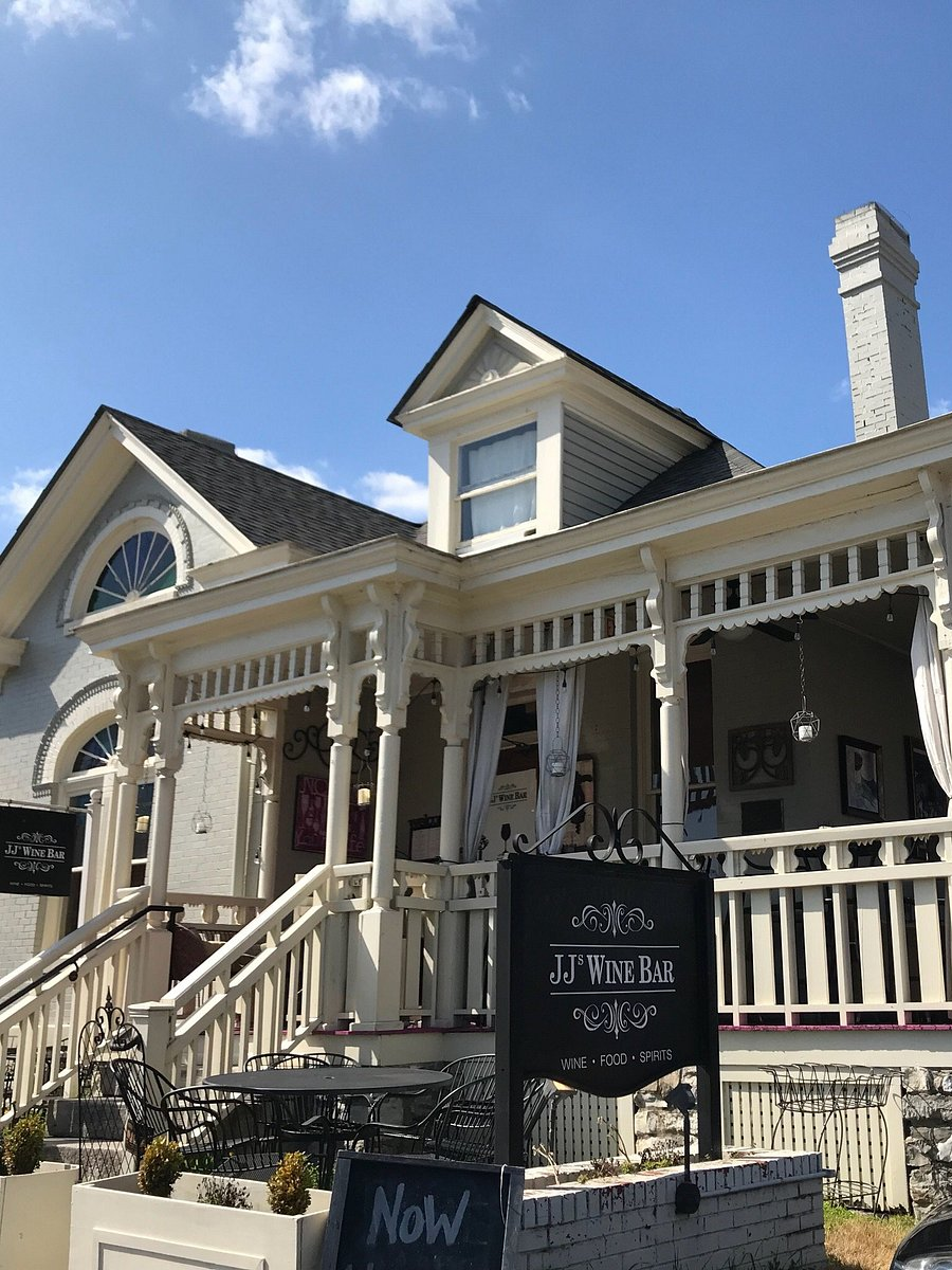 JJs Wine Bar Ila Bridal White Victorian-style building with a wraparound porch and JJ's Wine Bar sign; outdoor seating on the patio under a blue sky