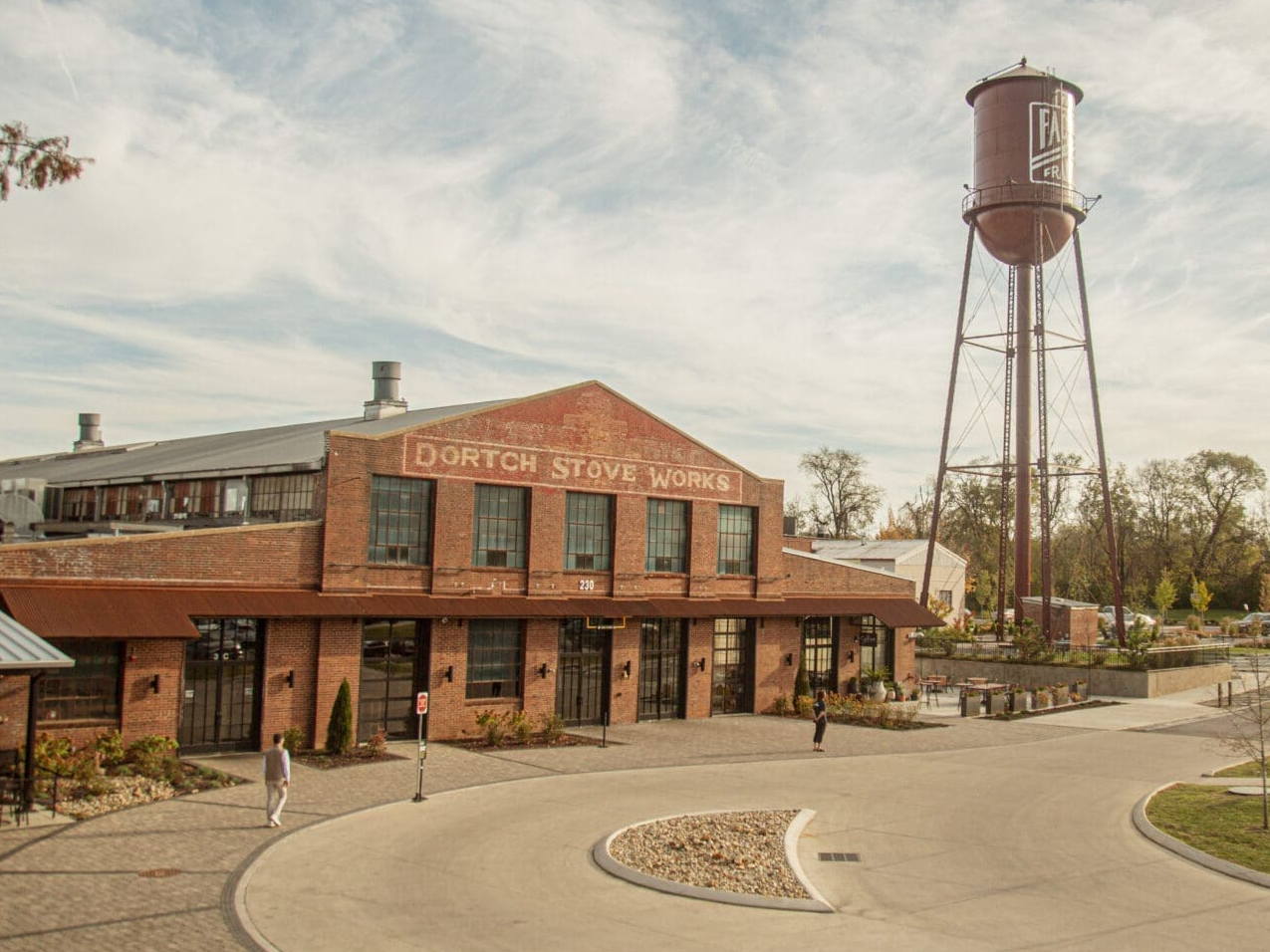 The Factory Ila Bridal Brick building labeled Dorch Stove Works beside a tall water tower in a small town plaza area.