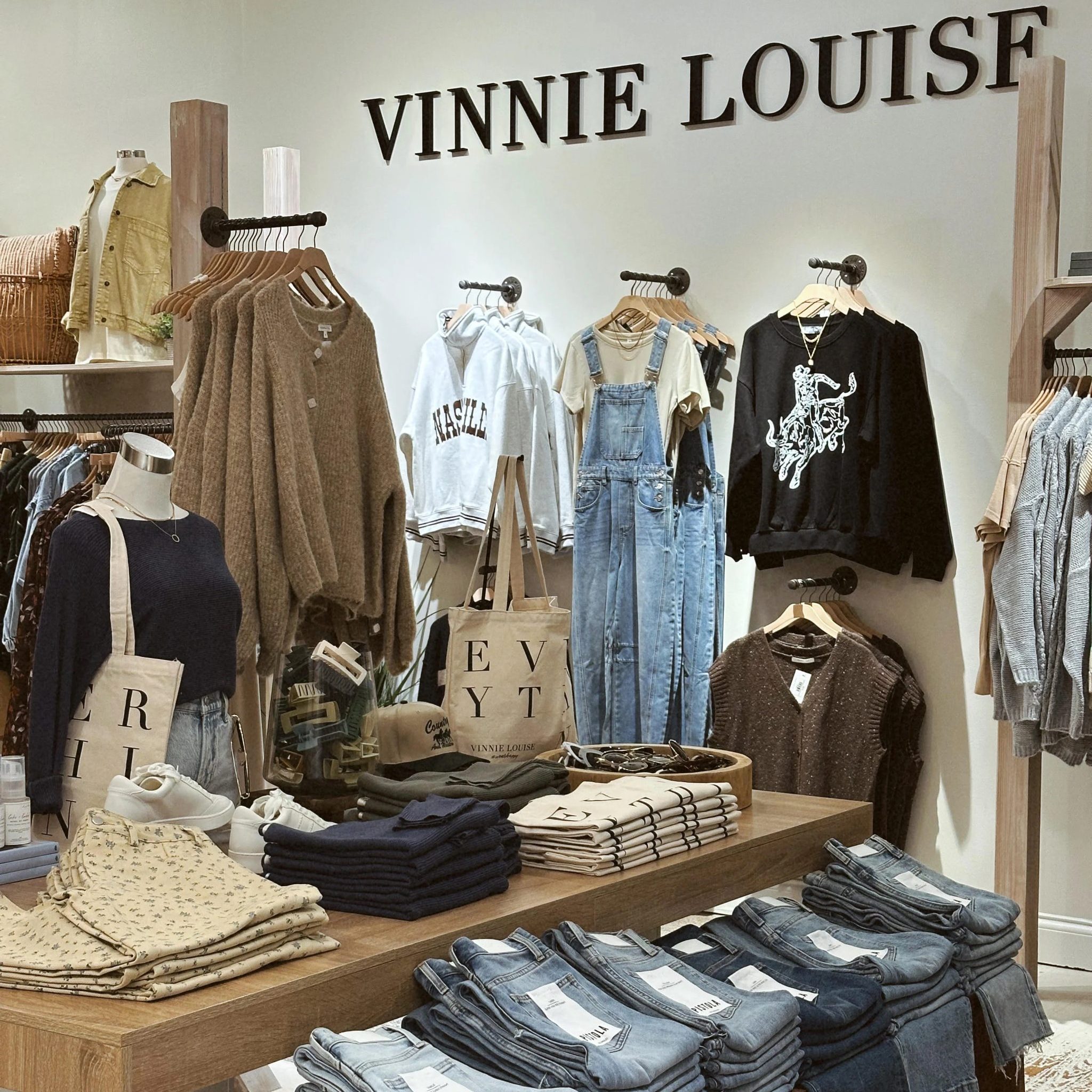 Vinny Louise Ila Bridal Clothing storefront display with jackets, sweaters, denim overalls, and folded jeans under a Vinnie Louise sign on the wall.